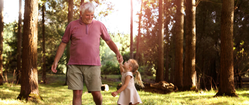 A grandfather holding hands with a little girl walking in a forest