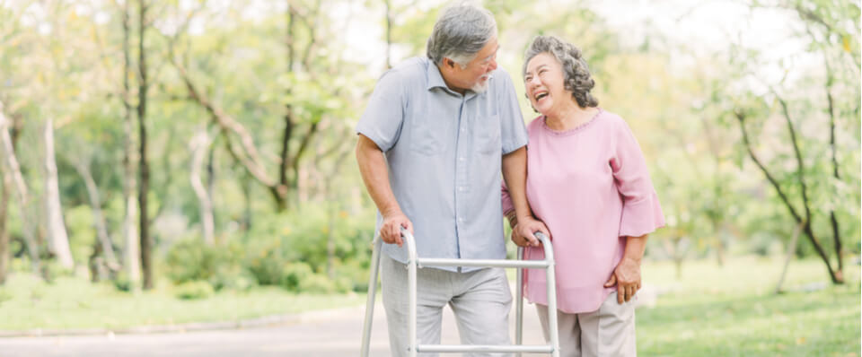 An older Asian couple walking happily together with the husband using a walker