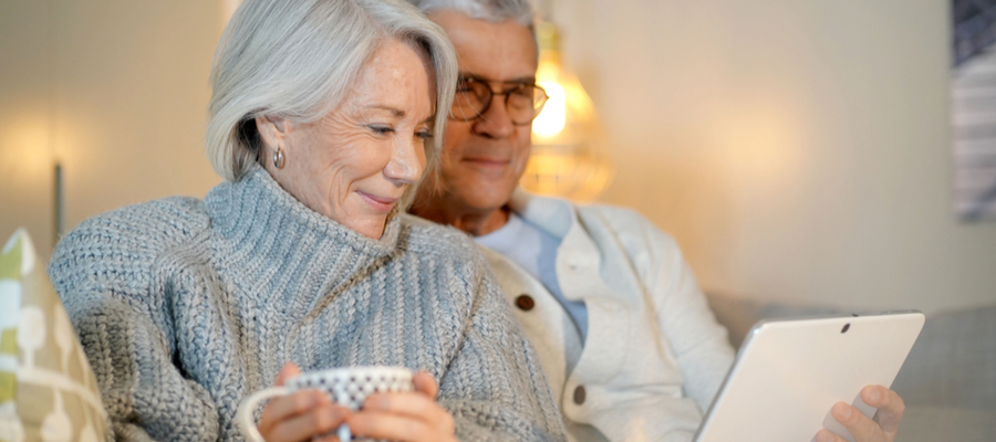 An older couple sitting on a couch smiling and looking at a device