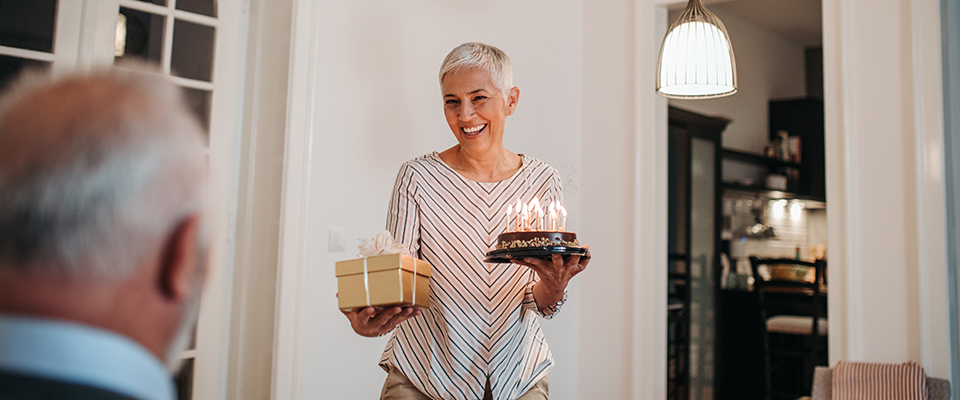 A woman holding a birthday cake with candles and a gift