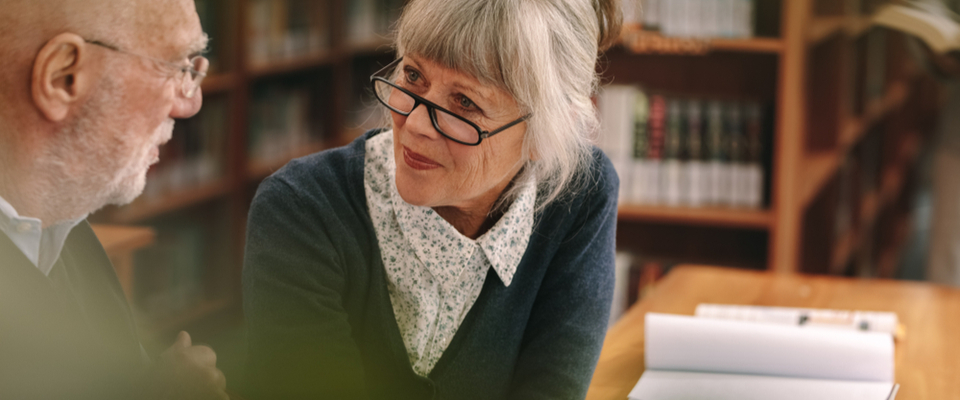 An older woman with glasses speaking with an older man at a library