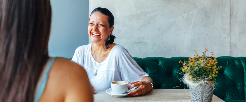 A woman in a white shirt laughing and talking holding a cup of coffee