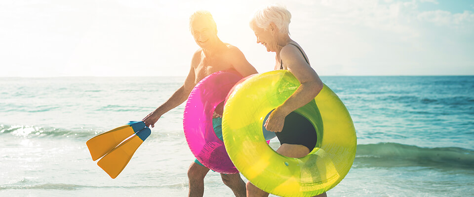 An older Canadian couple in their swimsuits on the beach, enjoying their vacation time mindful of the rules to saving on taxes.