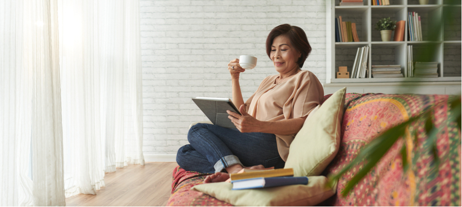 An older Asian woman sitting down with her tablet and a cup of coffee