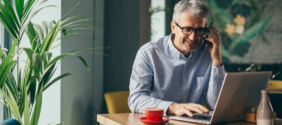 A man sitting a café working on his laptop and talking on his mobile phone