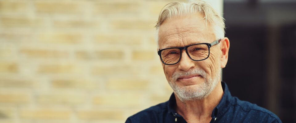 Landscape view of a man smiling at the camera wearing glasses and a blue collared shirt