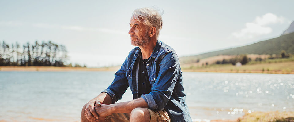 A man sitting by a lake looking off in the distance