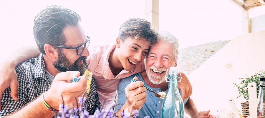 A teenage boy hugging his father and grandfather while eating outside