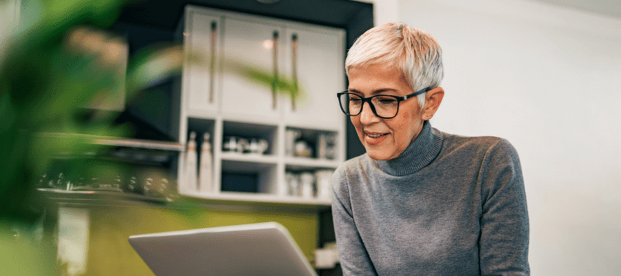 An older woman with short hair and glasses smiling and looking down at her laptop