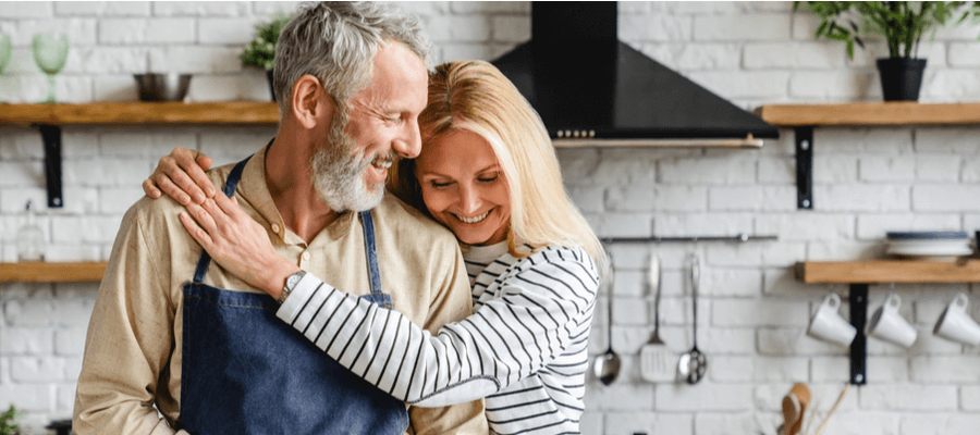 A happy couple laughing and smiling in the kitchen where the woman's arm is wrapped around the man