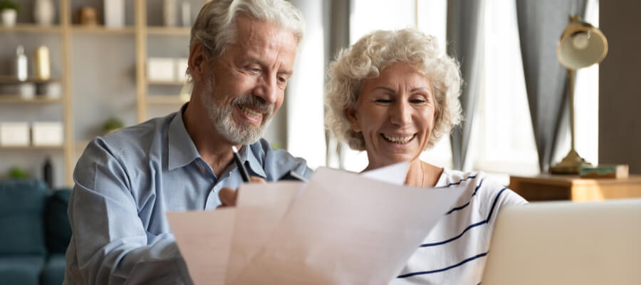 An older couple happily sitting at a laptop looking at documents together