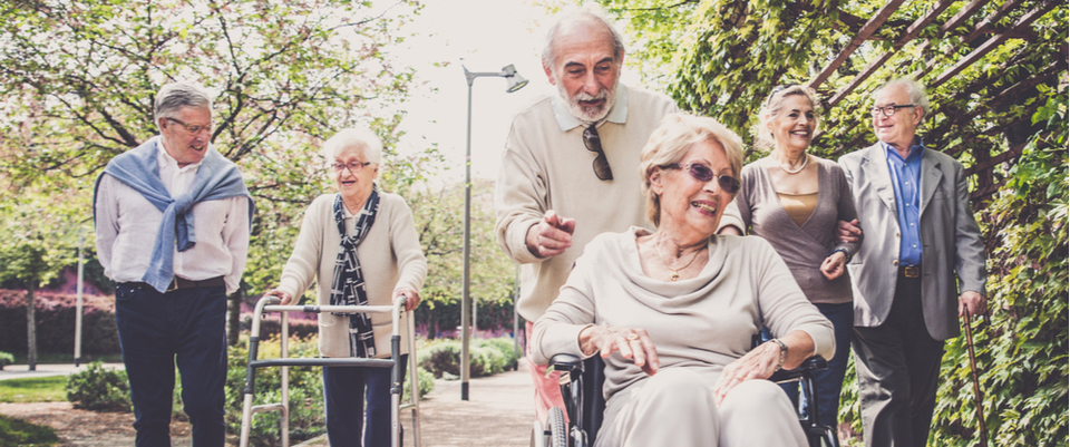 People walking down a path together where one is using a walker, another is using a cane and another sitting in a wheelchair