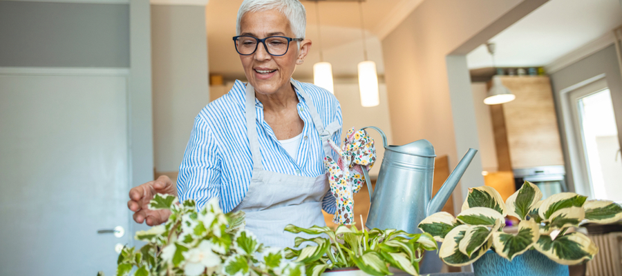 An older woman with glasses watering her plants