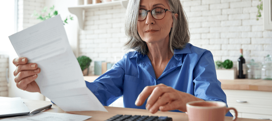 Older woman holding up a paper bill and using calculator to budget for the holiday season by utilising reverse mortgage funds.