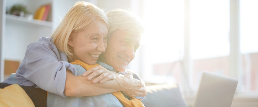 A woman wrapping her arms around her husband while looking at the laptop together