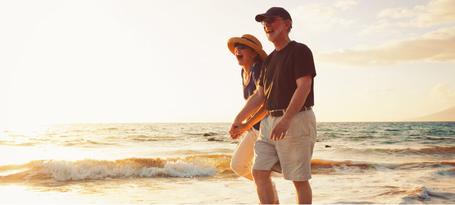 An older couple laughing and walking together on a beach by the water