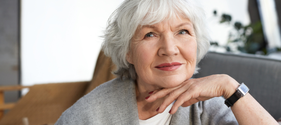 An older woman with short gray hair smiling at the camera with hand under her chin