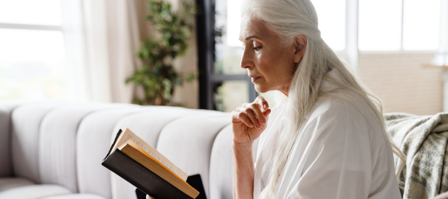 Older woman with long hair reading a book on her couch