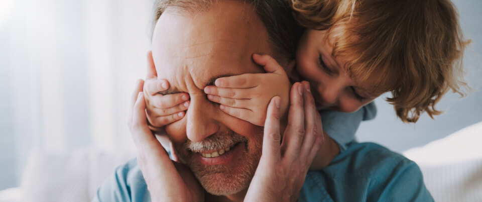 A toddler covering the eyes of a man from behind
