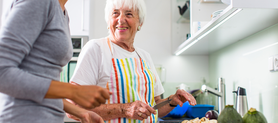 An older woman wearing an apron and cooking talking to someone