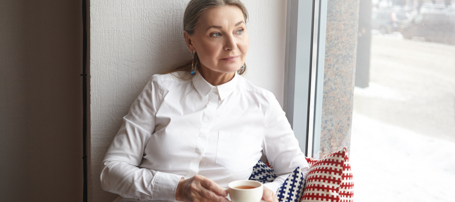 A woman sitting by a window holding a cup of tea looking out the window