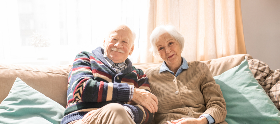 An older couple sitting on a couch smiling at the camera