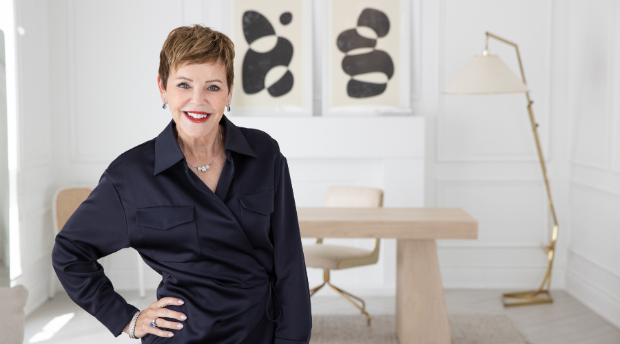 A woman named Pattie Lovett Reid stands in the foreground of a home office, with a white desk, chair, and some artwork behind her.