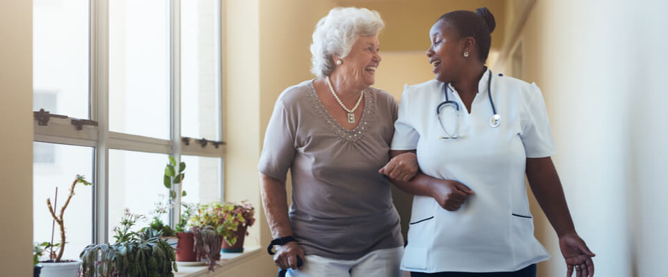 An older woman walking with a cane talking happily with a caregiver