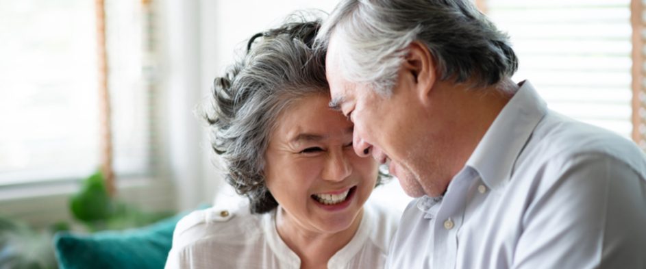 An older Asian couple smiling at each other with foreheads touching