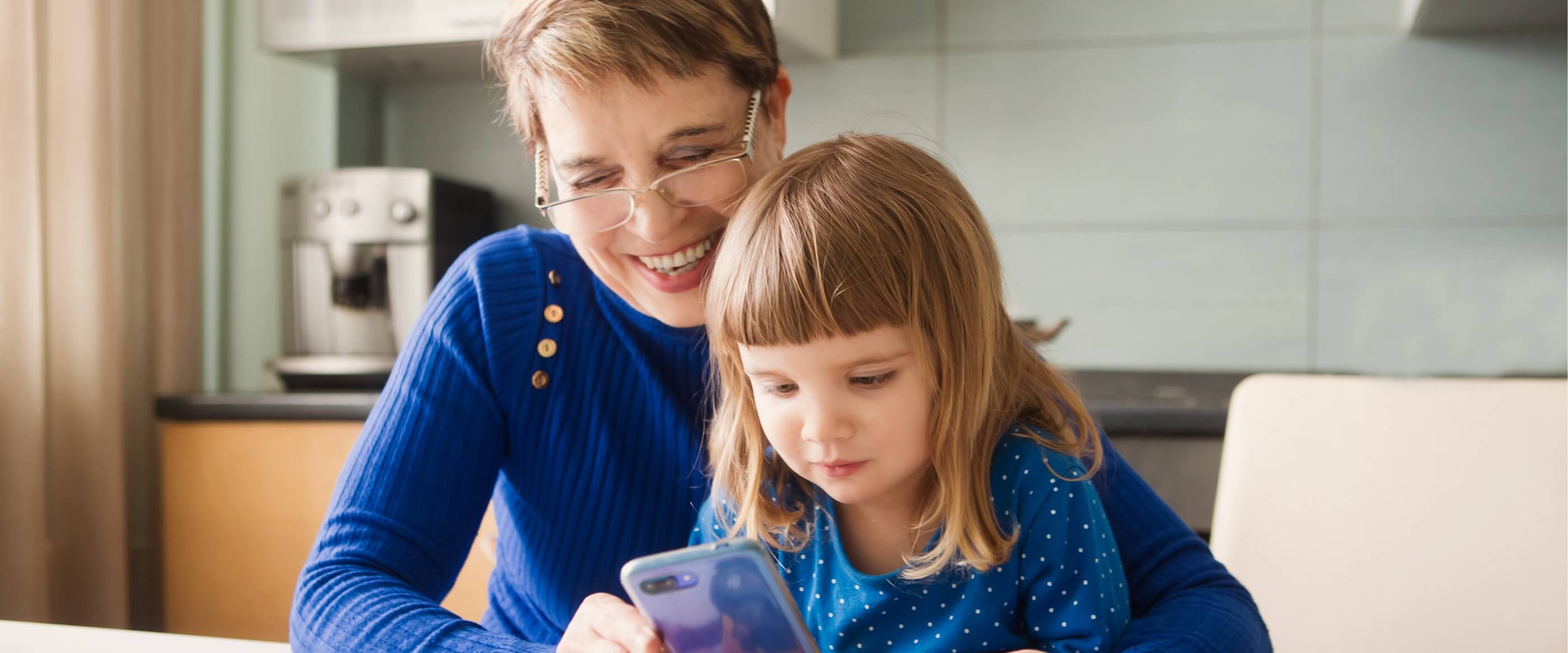 A grandmother holding a mobile phone with her young granddaughter