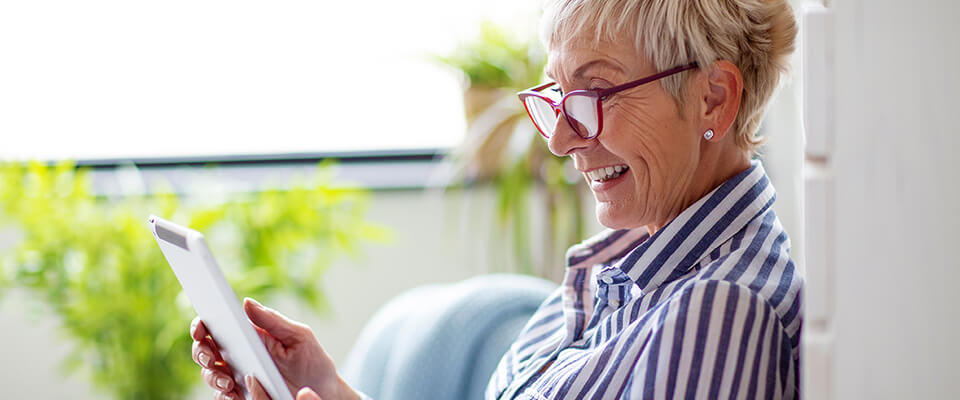 An older woman wearing red glasses happily looking at her tablet out by her balconey