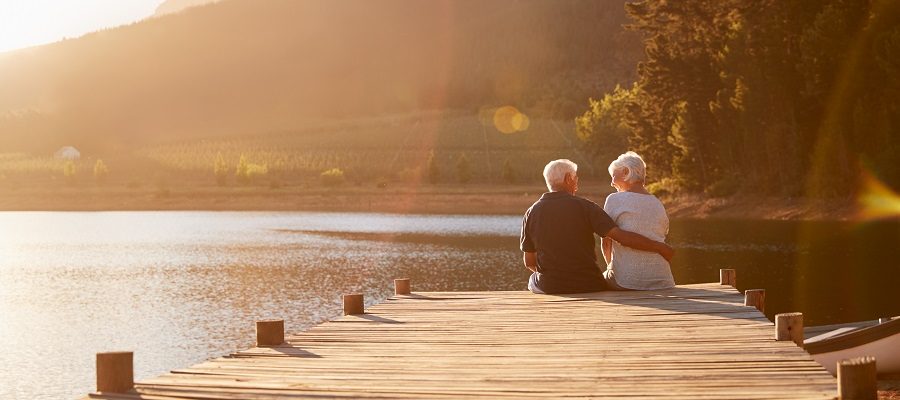 A view of an older couple sitting on the edge of dock by the lake