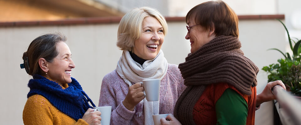 Three women standing outside smiling and talking holding coffee cups