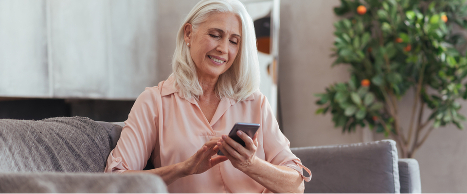 An older woman sitting on a couch looking down at her mobile phone