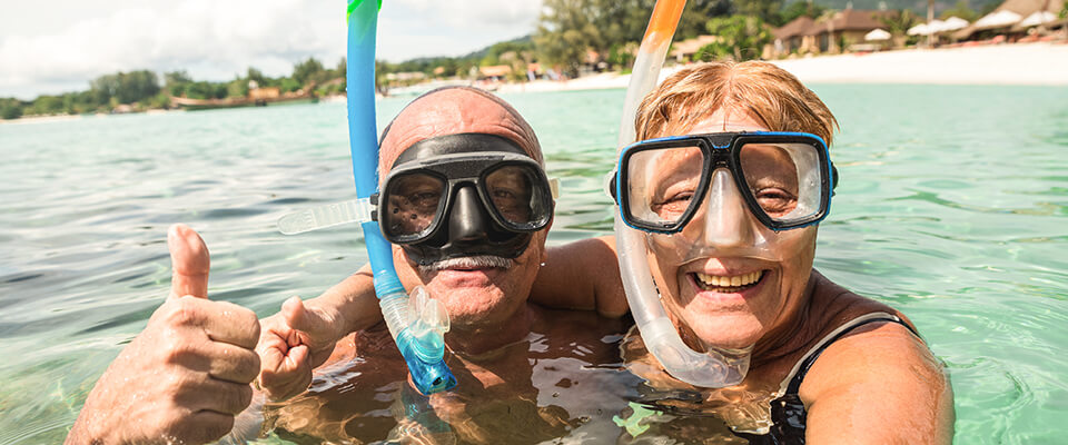 An older couple swimming in the ocean wearing snorkel goggles