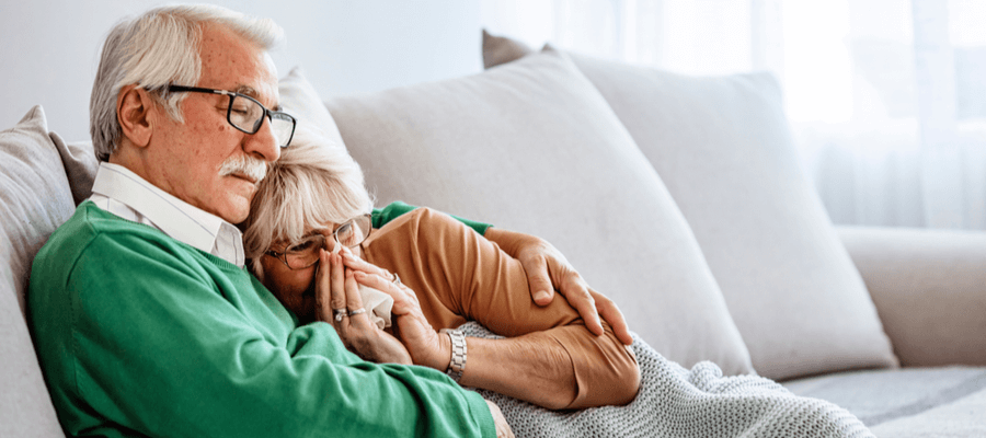 An older man holding his wife who is holding a tissue sitting on a couch