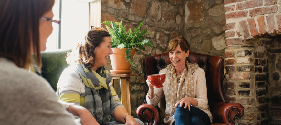 Three woman talking and laughing together while one is holding a large coffee cup