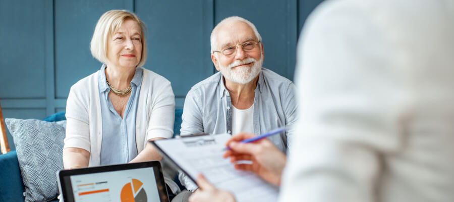 An older couple sitting with a person taking their information on a clipboard