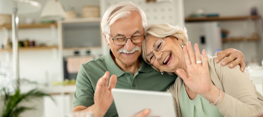 An older couple waving hi and smiling and holding a tablet