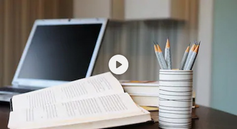 video image still of a laptop, a book and a pencil holder full of pencils