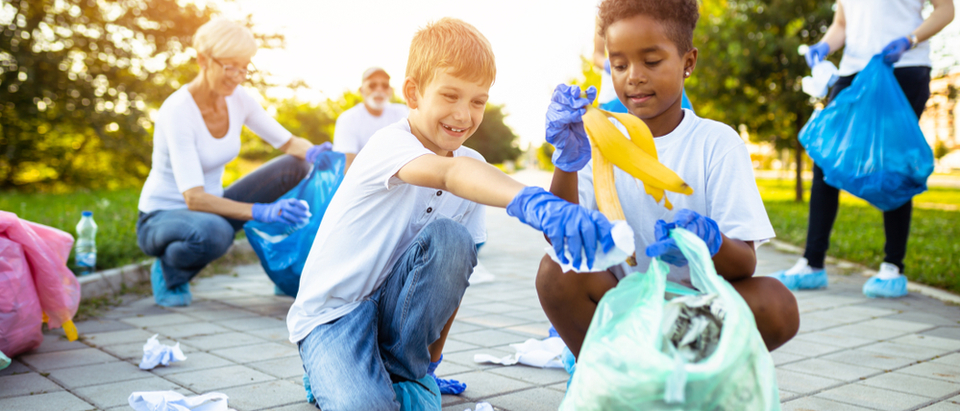 Two young boys picking up garbage into a plastic bag wearing plastic blue gloves