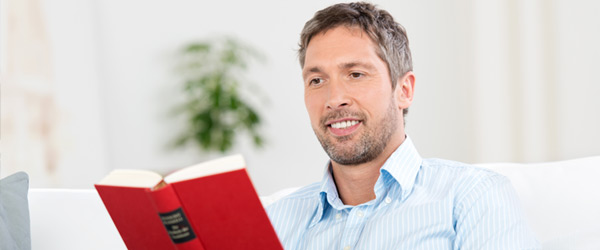 Man enjoying the benefits of a Canadian reverse mortgage his elders opted for Man comfortably seated and reading a book in a house, happy with the security provided by the Canadian reverse mortgage his elders opted for.