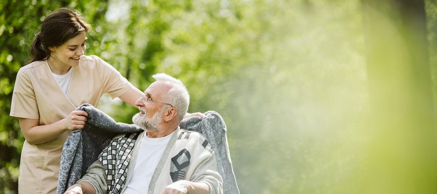 A nurse or caregiver wrapping a blanket to an older man sitting down